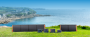 Solar panels set up on grass with a scenic ocean view in the background